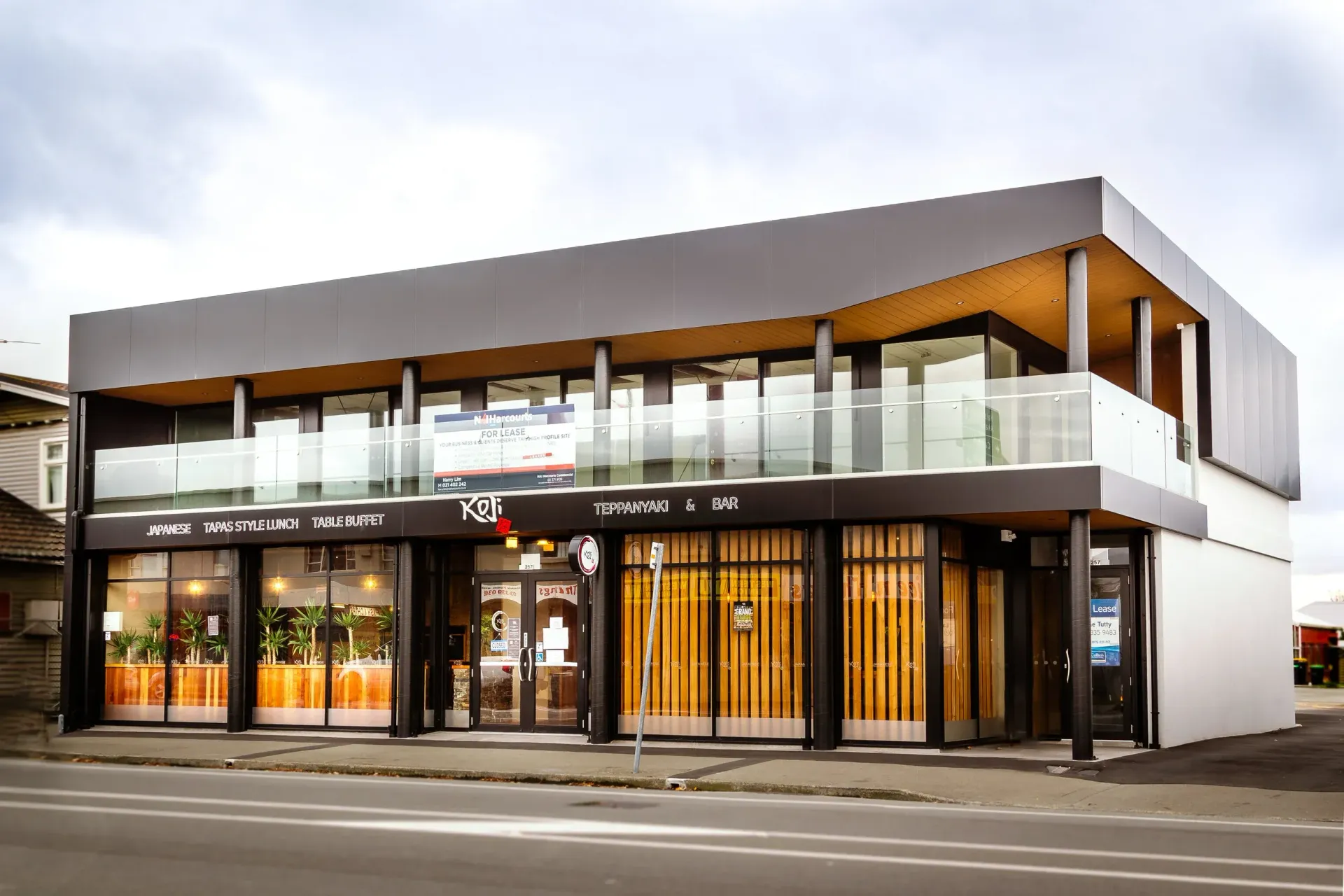 Blue commercial building with multiple windows and a small front garden, overcast sky.