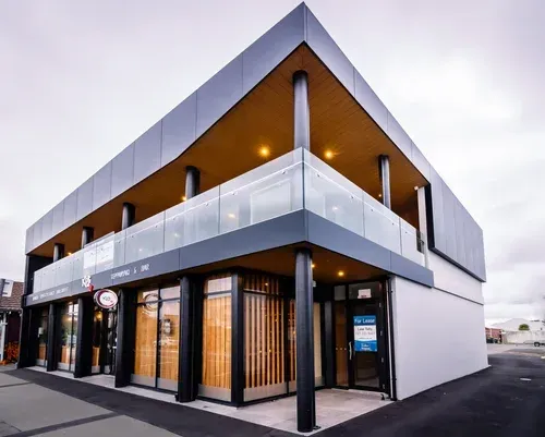 Modern two-story building with glass balconies, black trim, and a wooden facade.