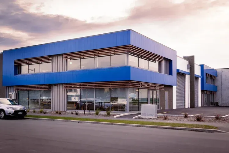 Modern two-story commercial building with blue facade and large windows. A car is parked in front.
