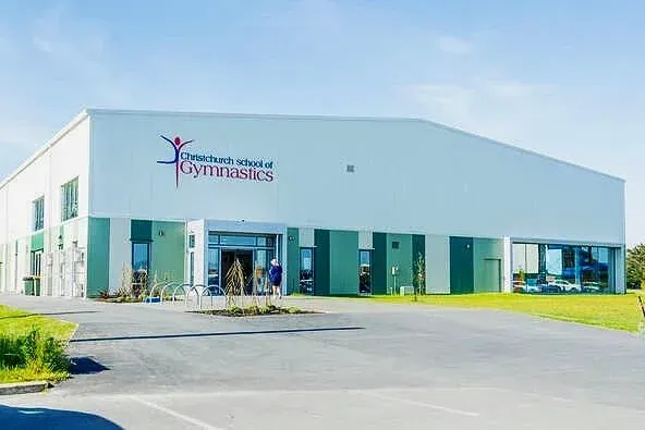 White and green gymnastics building with blue sky and parking lot.