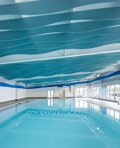 Indoor swimming pool with turquoise water and decorative wave-patterned ceiling.