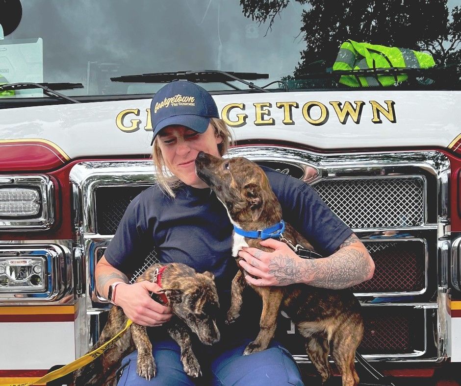 A woman is holding two dogs in front of a Georgetown fire truck