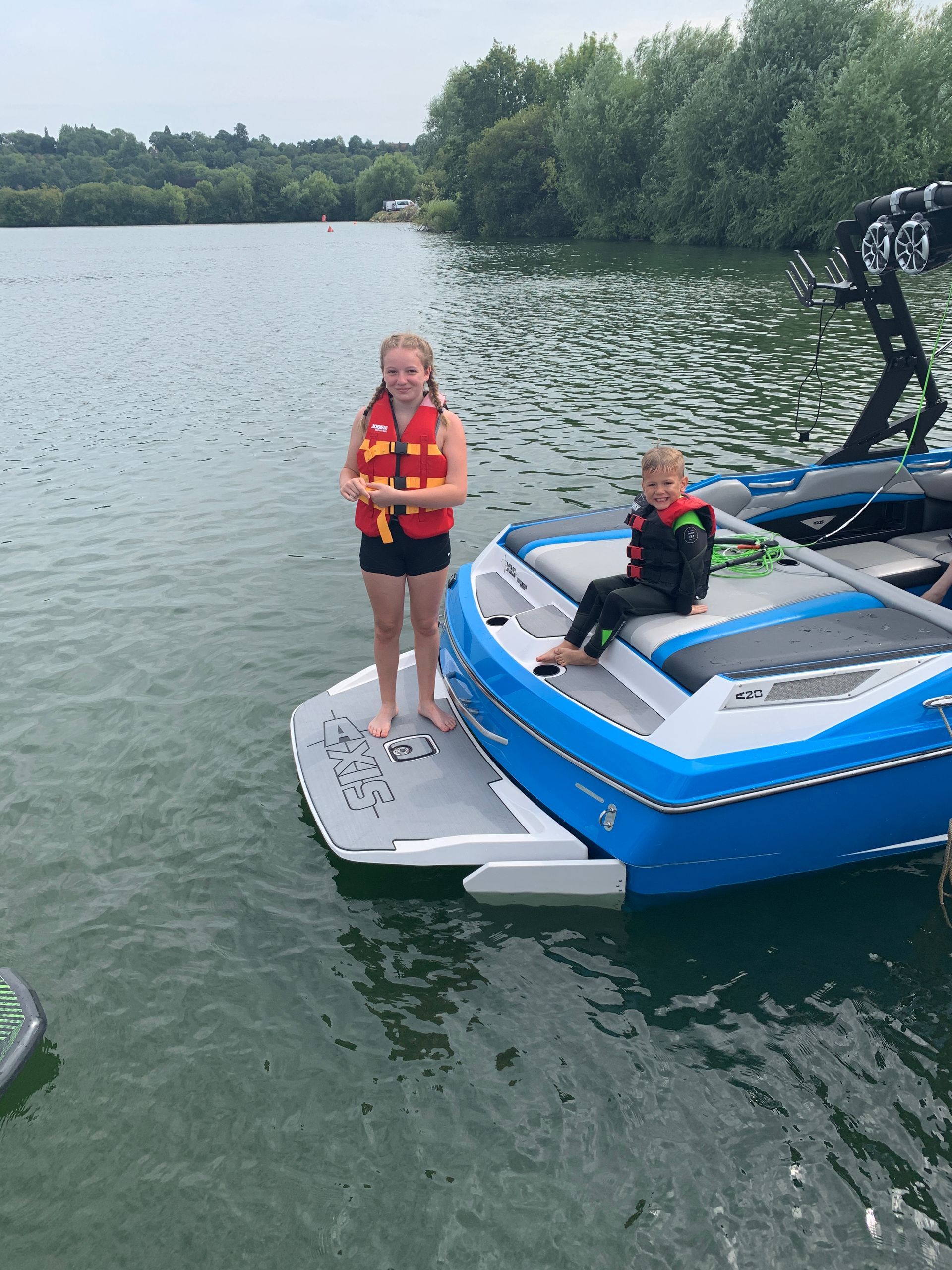 A girl and a boy are standing on a boat in the water