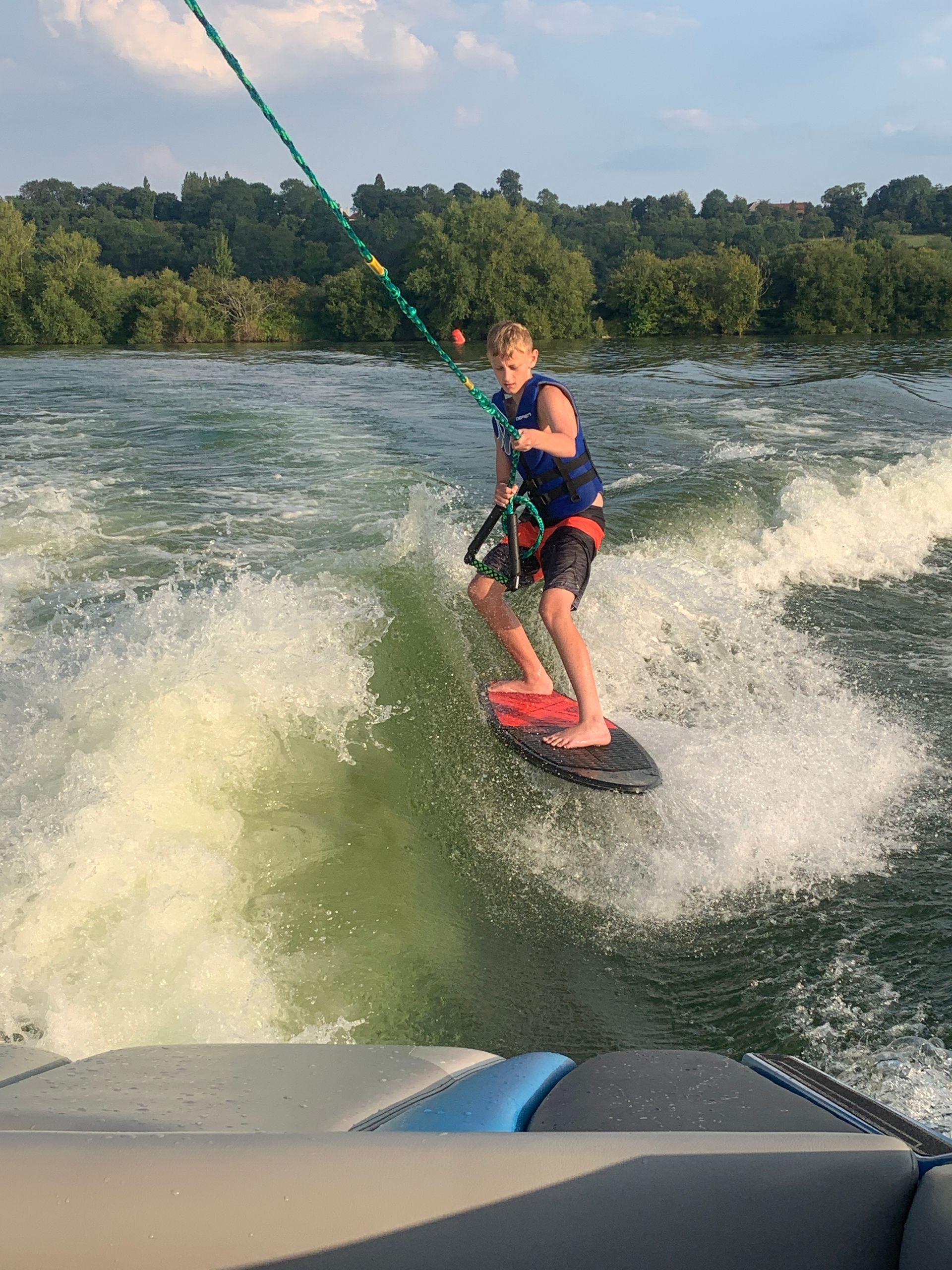 A young boy is riding a wave on a wakeboard on a lake.