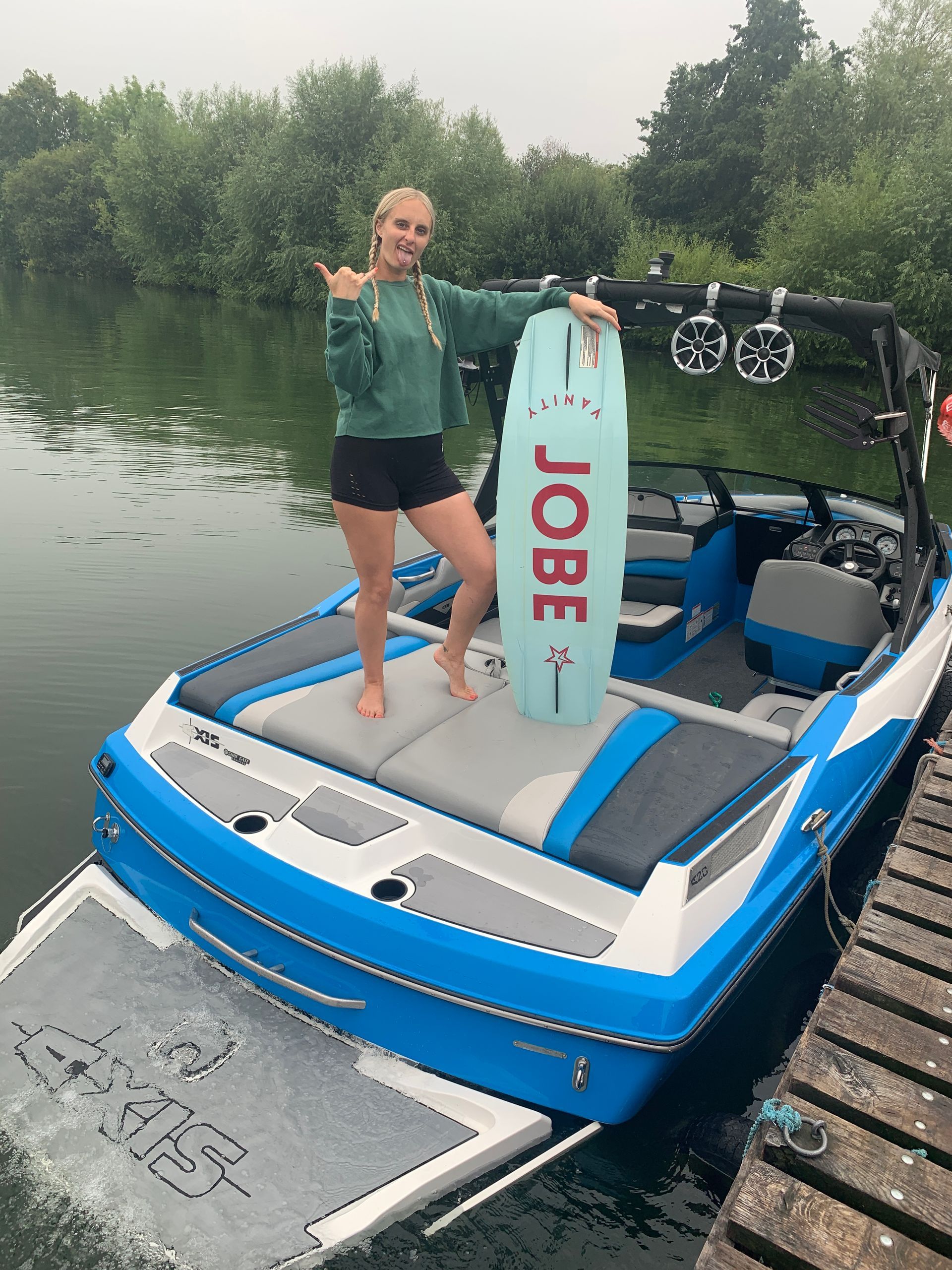 A woman is standing on a boat holding a jobe wakeboard.