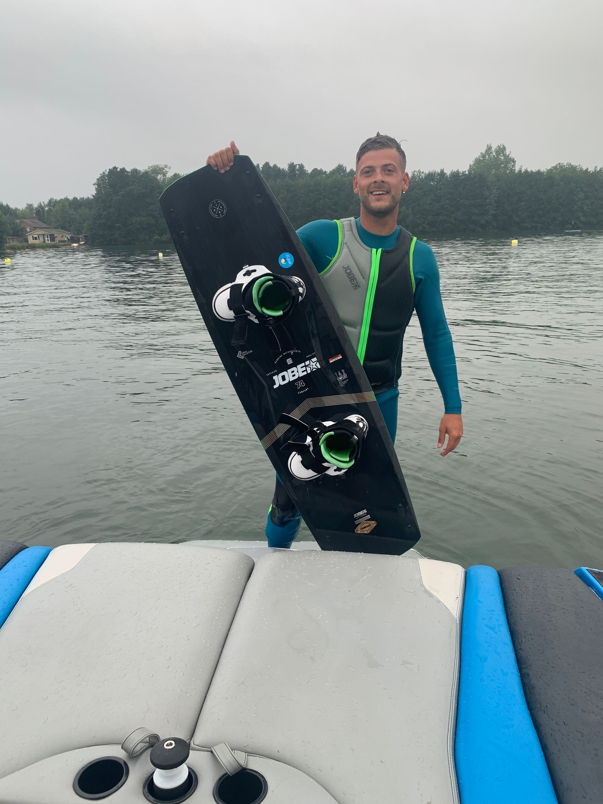 A man is standing on the back of a boat holding a surfboard.