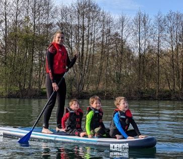 A woman and three children are on a paddle board in the water.