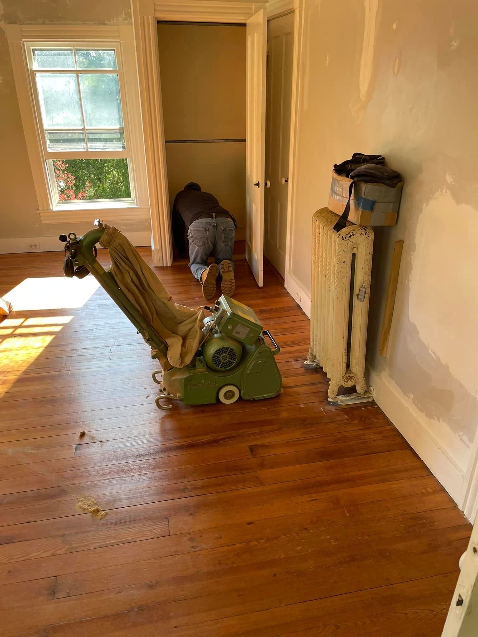 A person is sanding a wooden floor with a machine in a room.