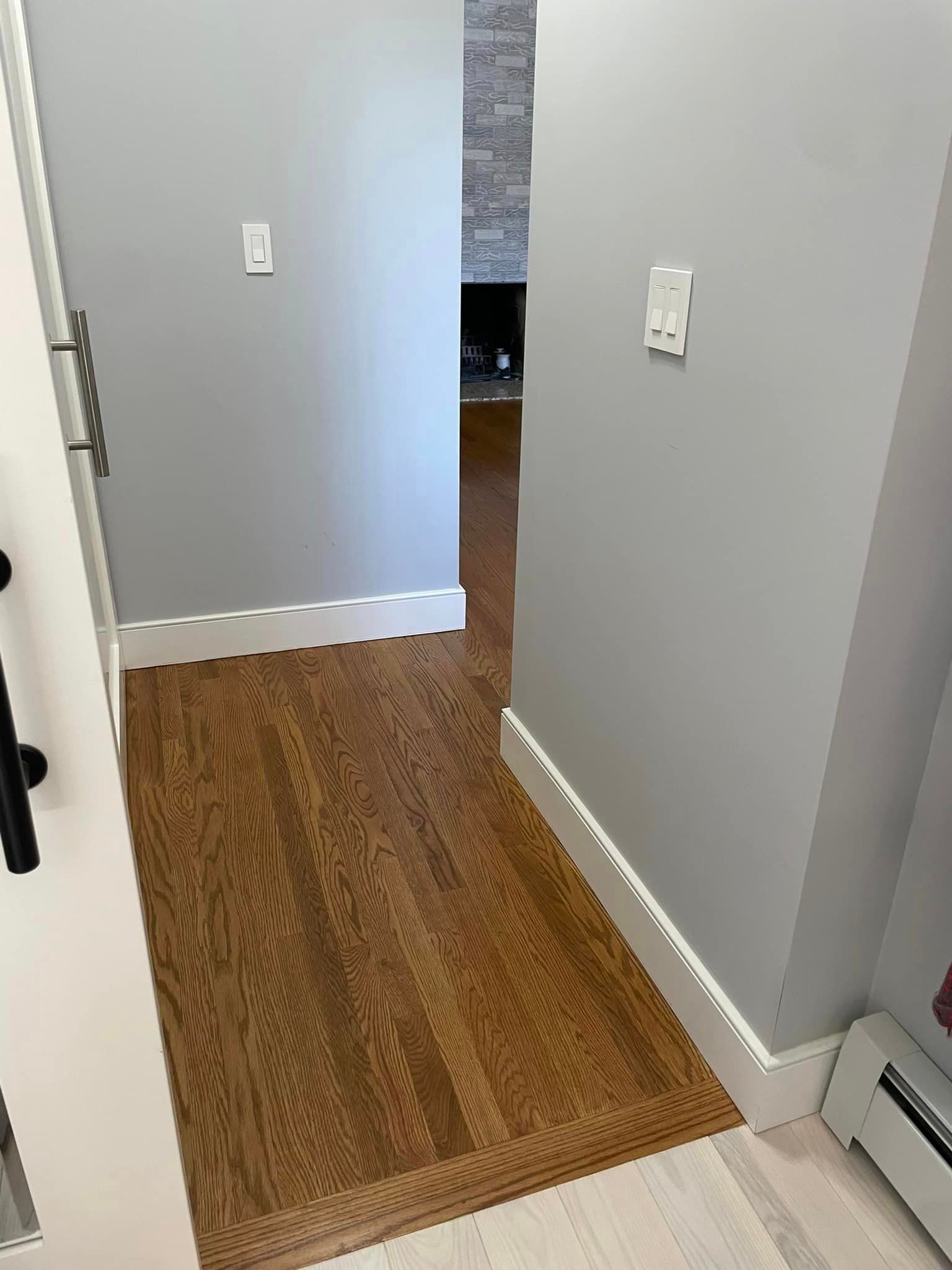 A hallway with hardwood floors and gray walls leading to a living room.