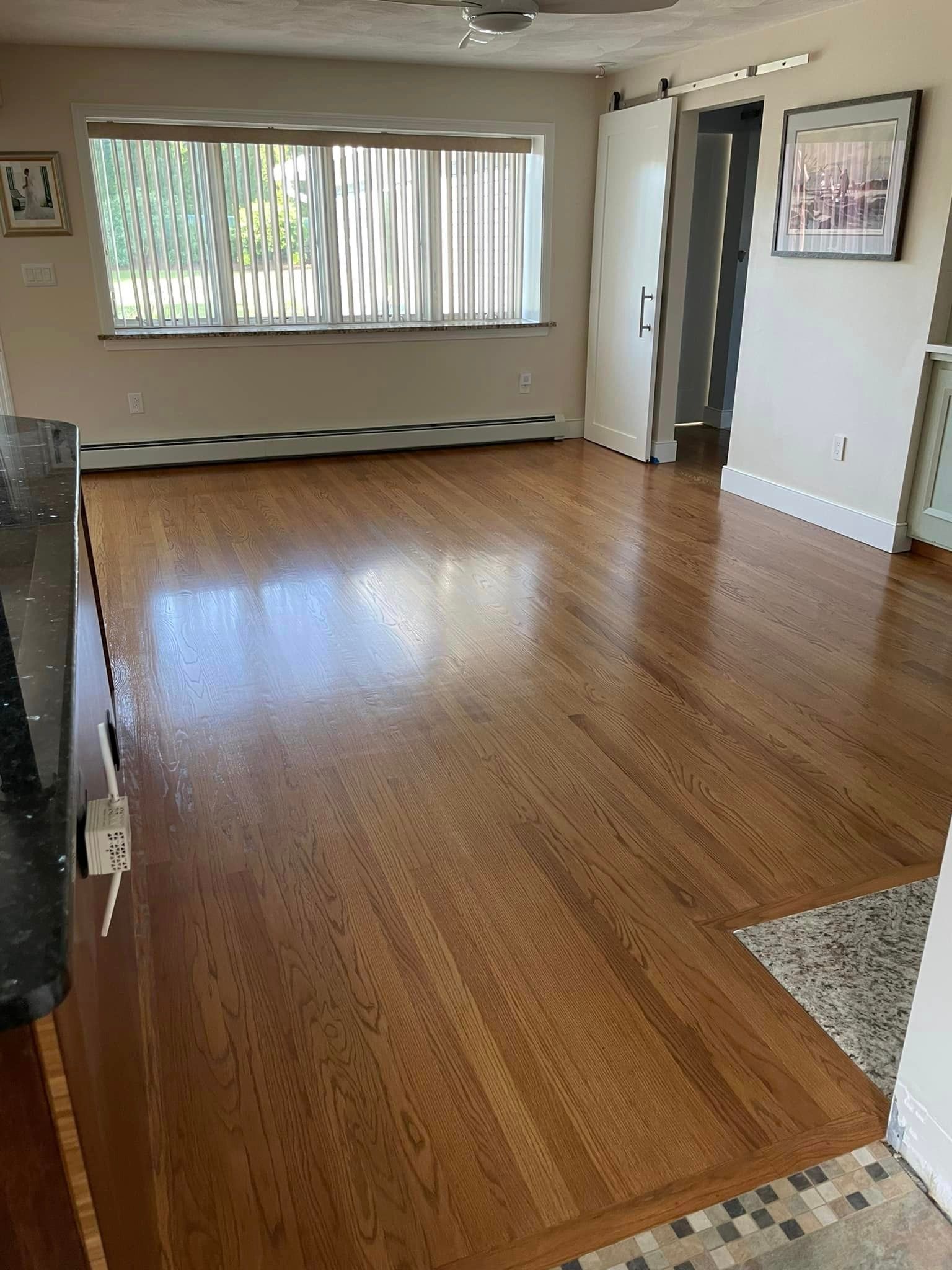 An empty living room with hardwood floors and a large window.