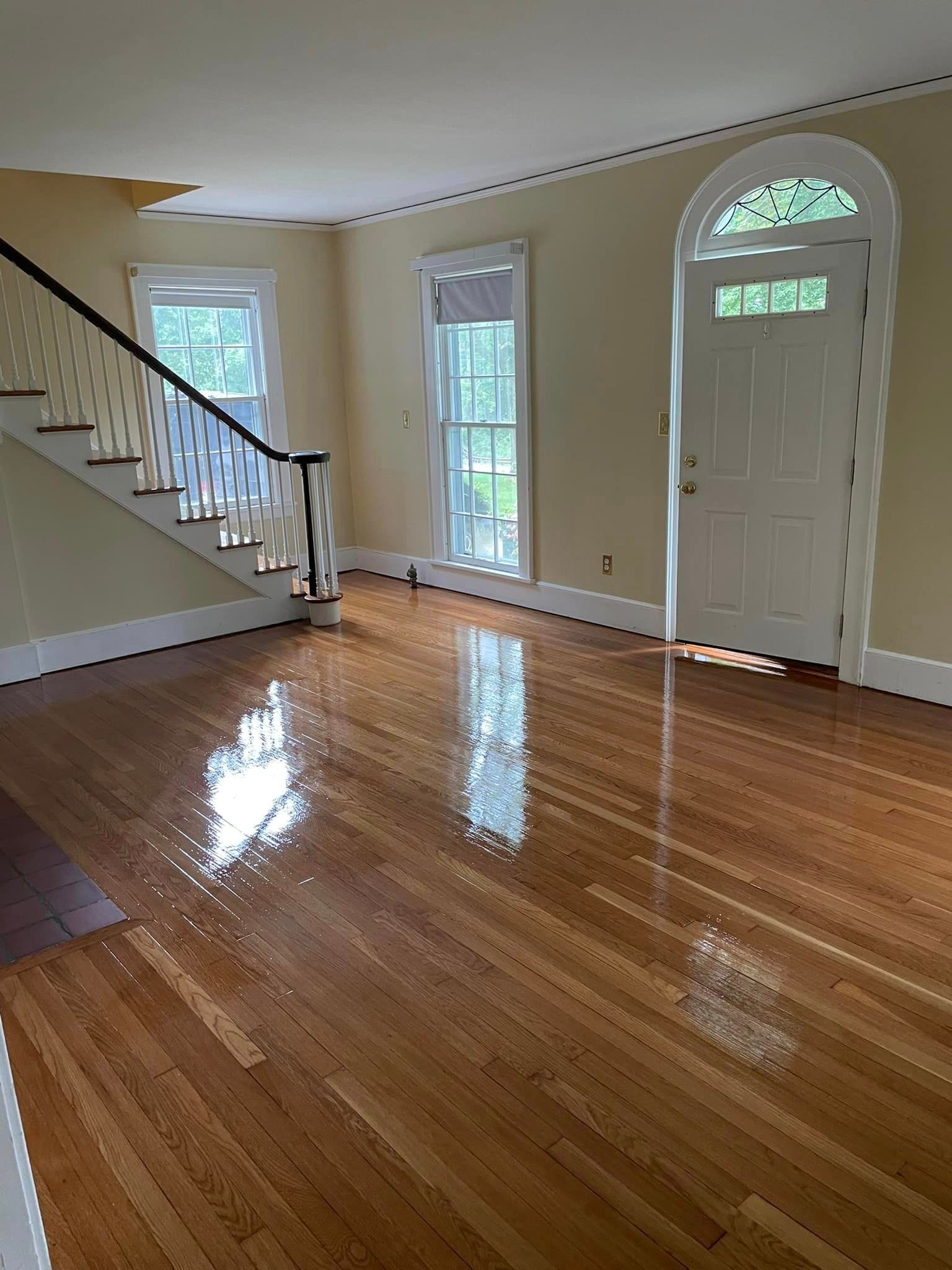 An empty living room with hardwood floors , stairs , and a door.