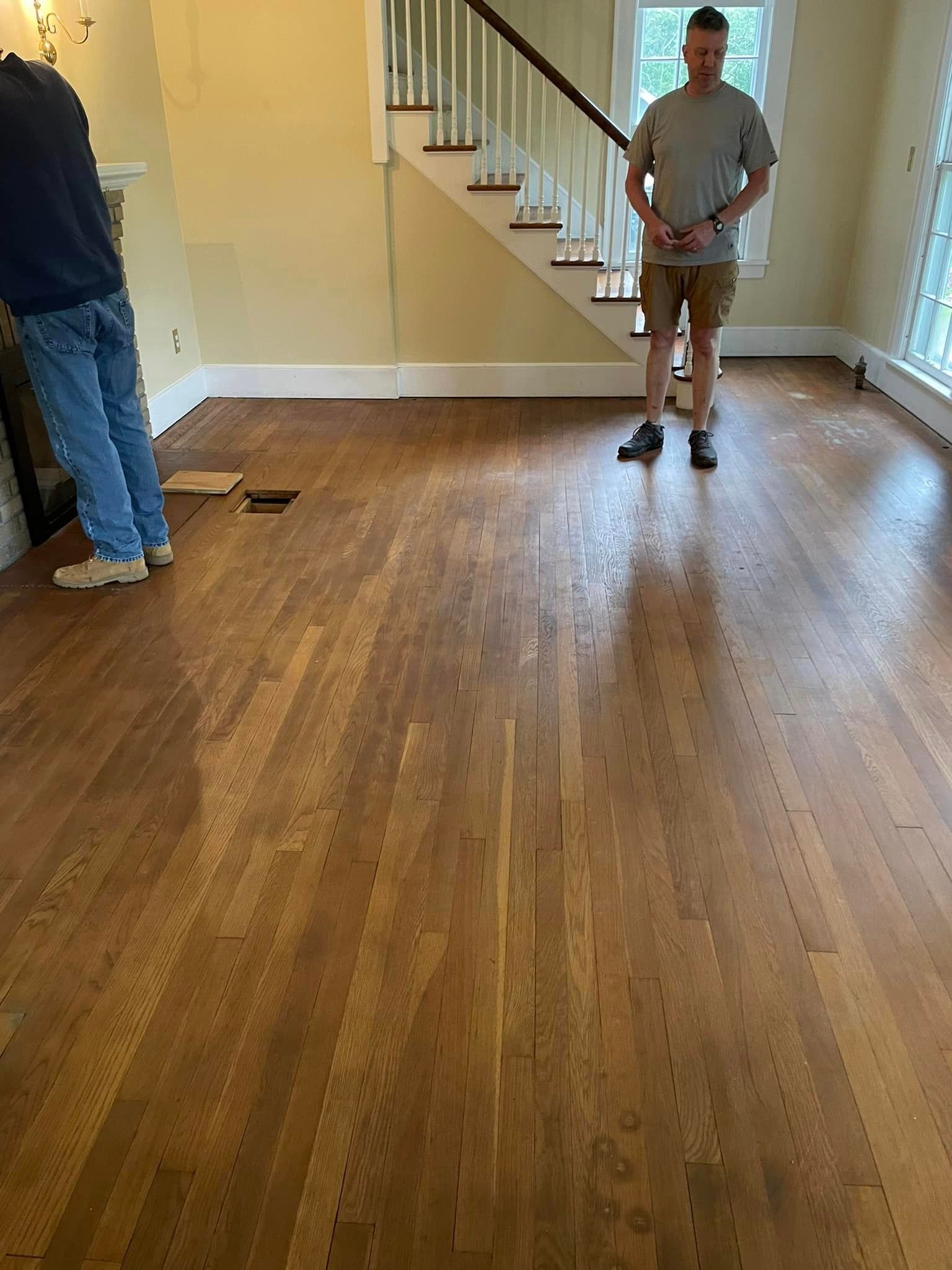 A man is standing on a wooden floor in a living room next to a staircase.