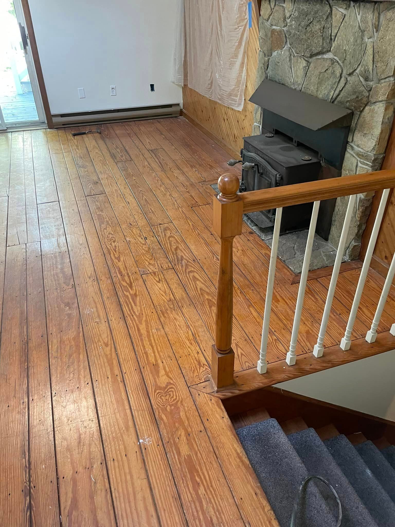 A wooden floor with stairs and a fireplace in the background.
