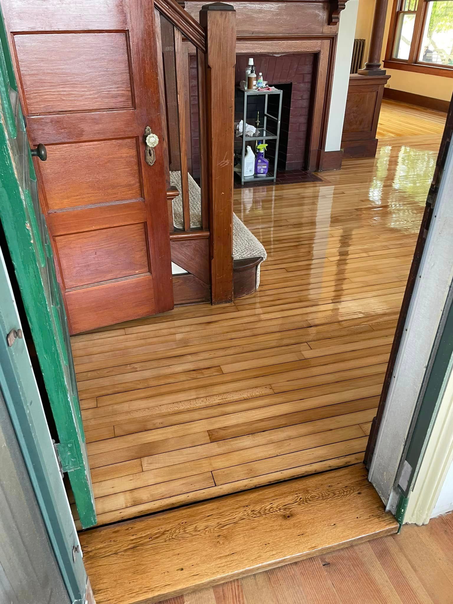 A wooden floor in a living room with a fireplace and stairs.