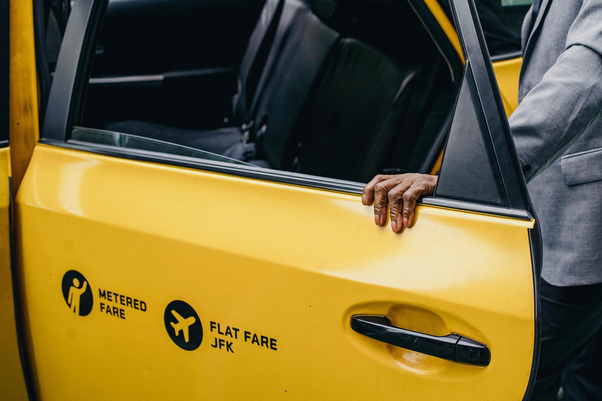 Een man in pak leunt tegen de deur van een gele taxi.