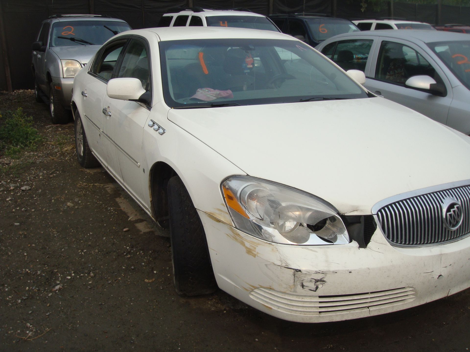A white buick is parked in a lot with other cars
