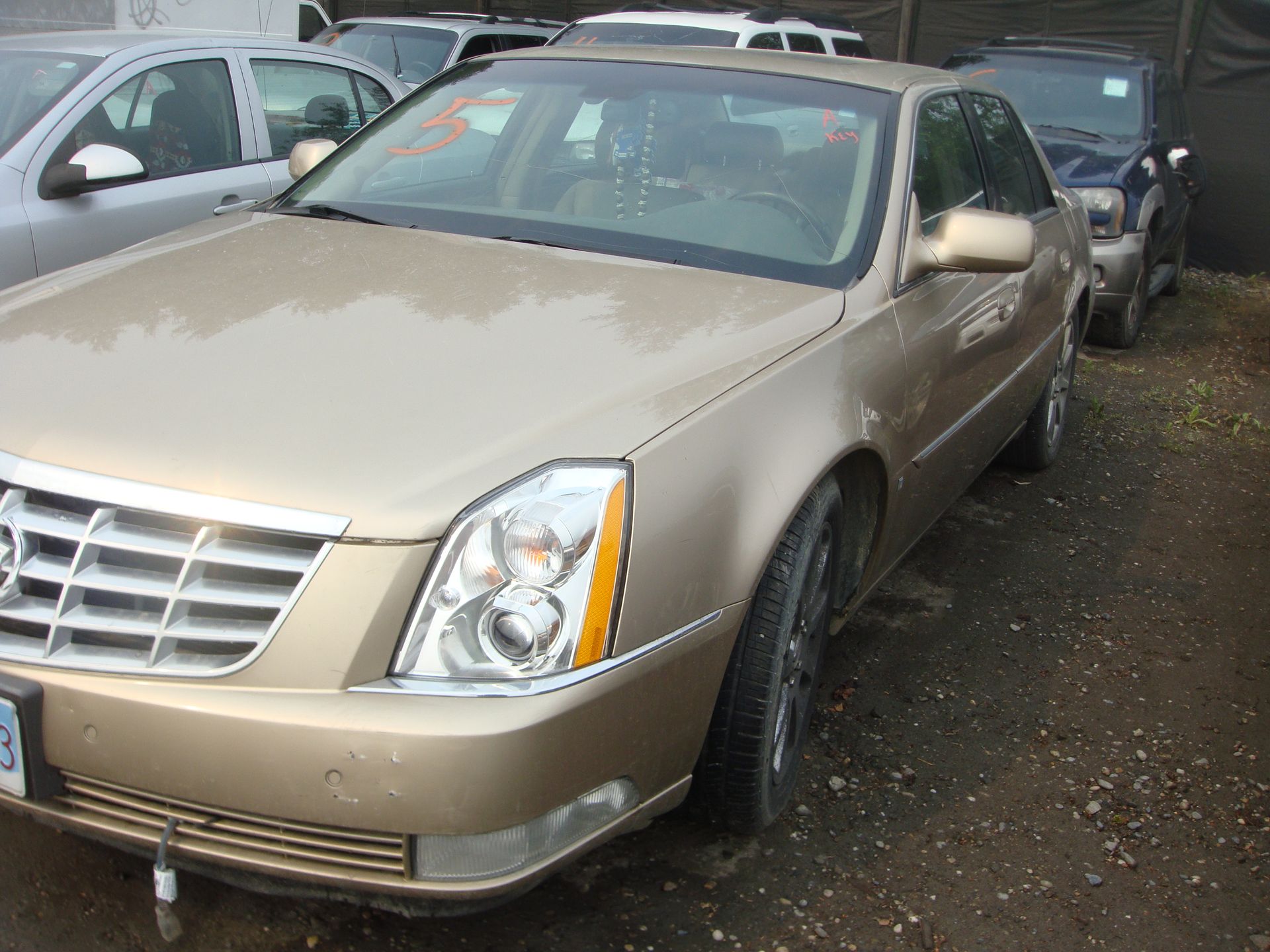 A gold cadillac is parked in a lot with other cars