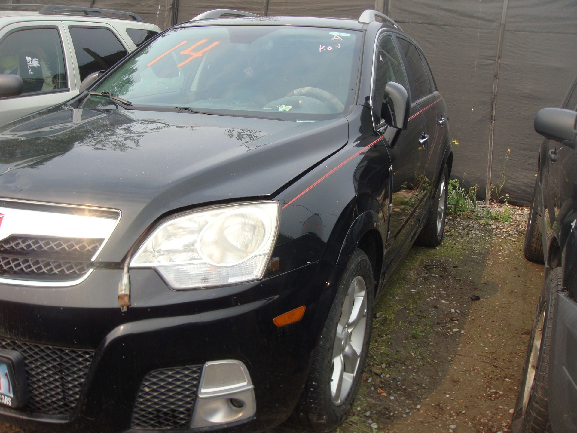A black car is parked in front of a fence.