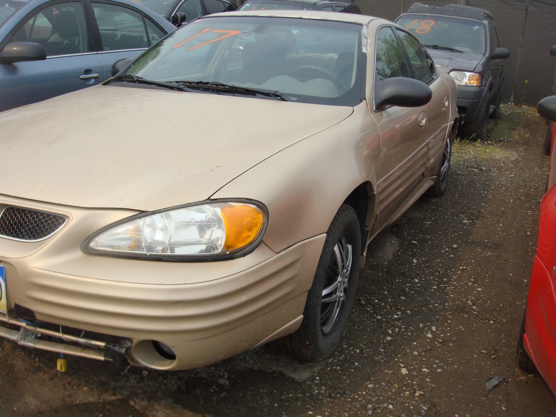 A tan car is parked next to a red car