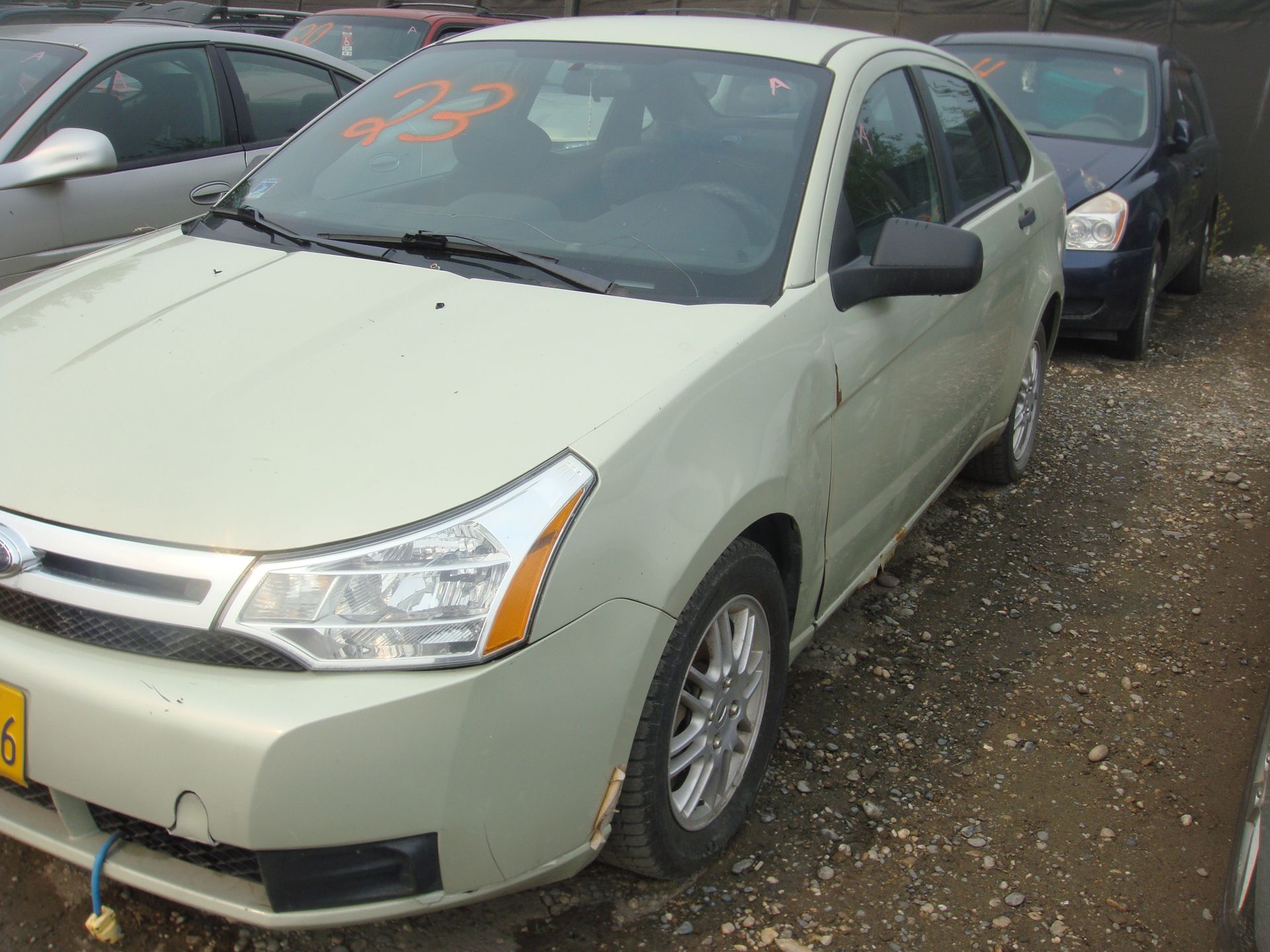A white ford focus is parked in a gravel lot