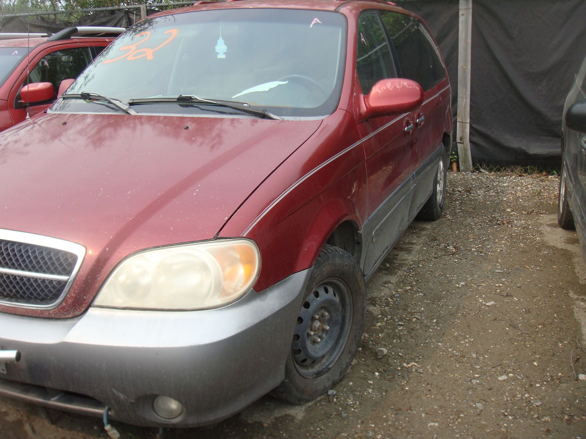 A red minivan is parked in a gravel lot