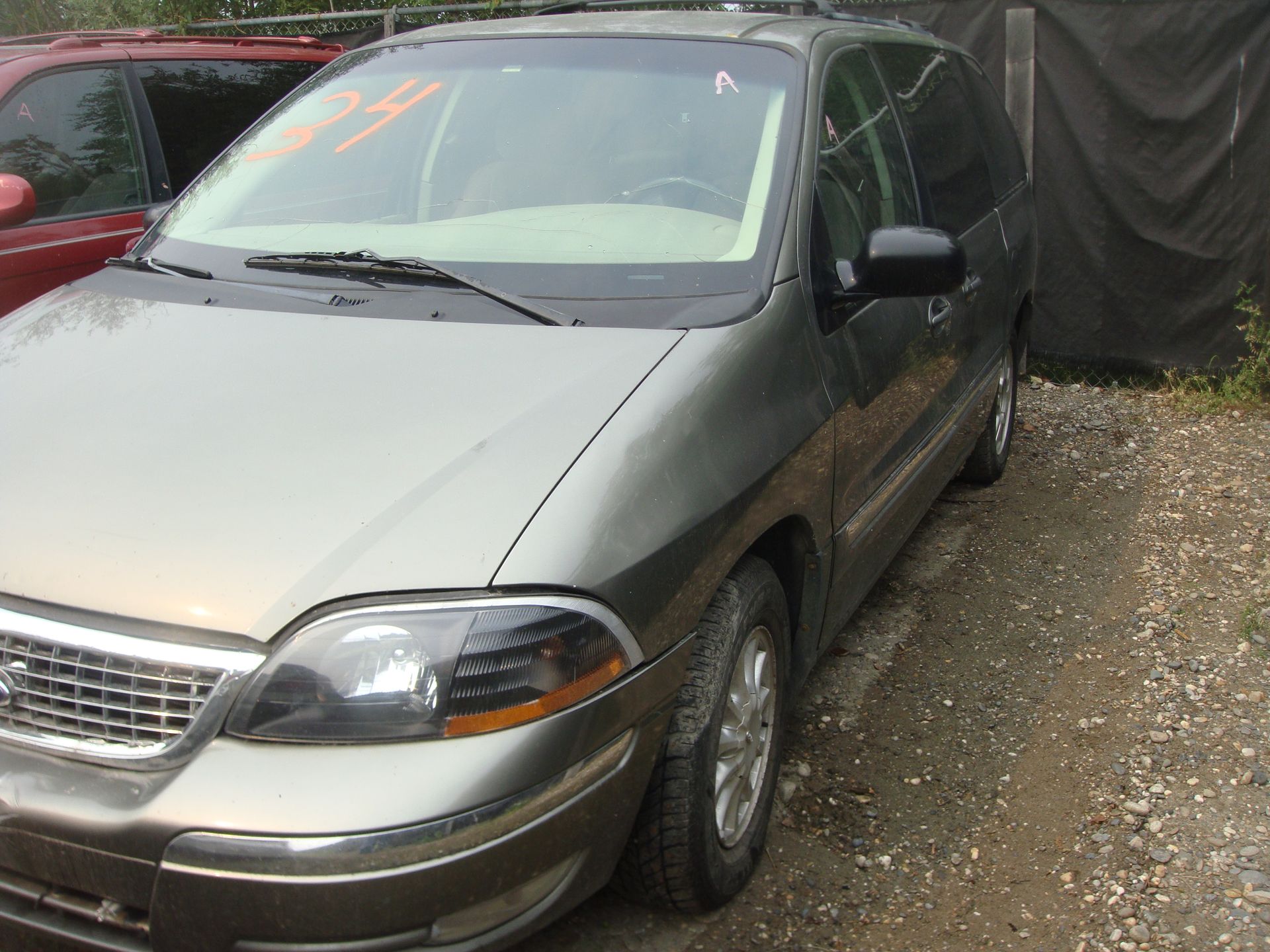 A grey ford minivan is parked in a gravel lot