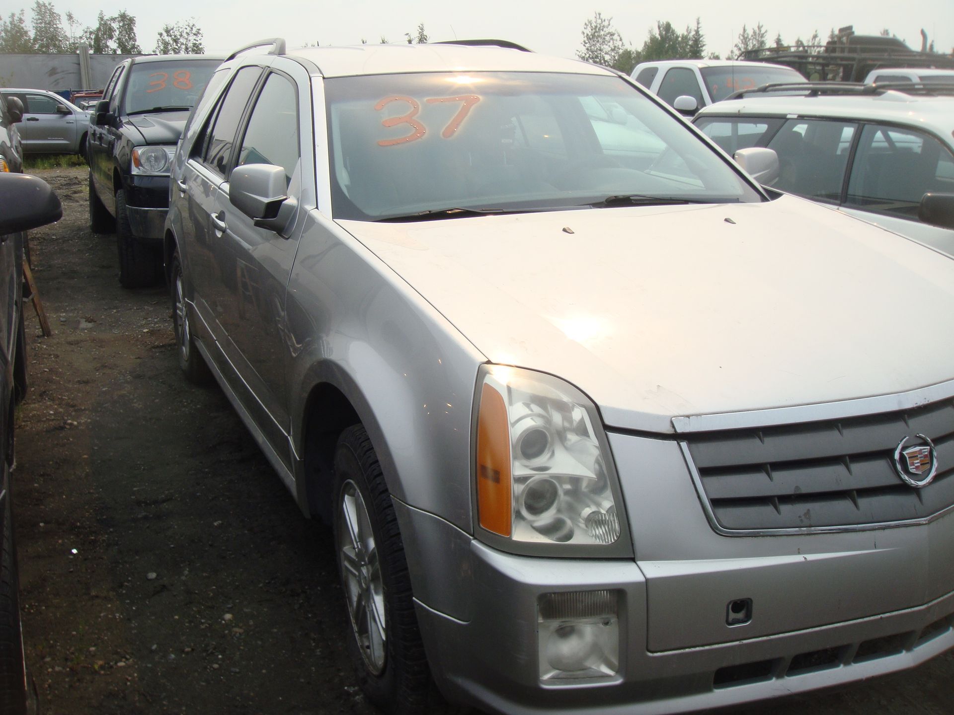 A silver cadillac is parked in a lot with other cars