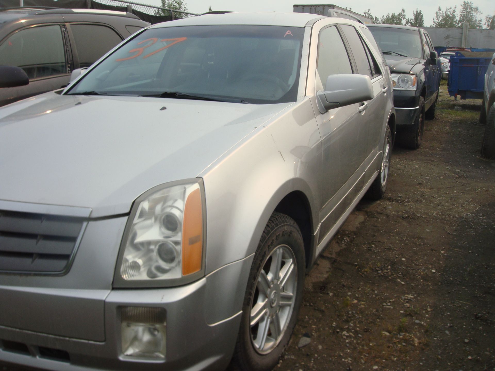 A silver cadillac is parked in a gravel lot