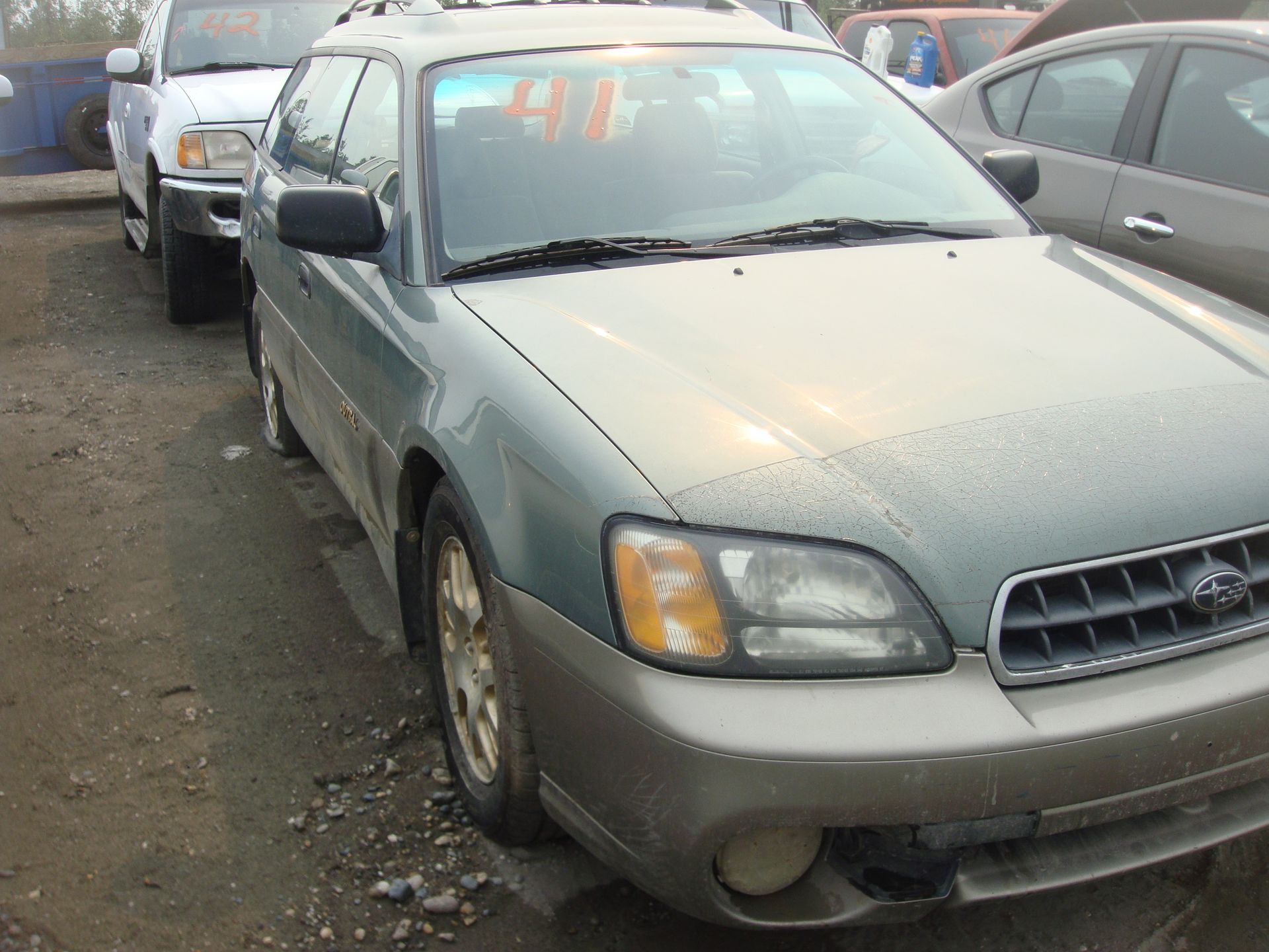 A green subaru is parked in a lot with other cars