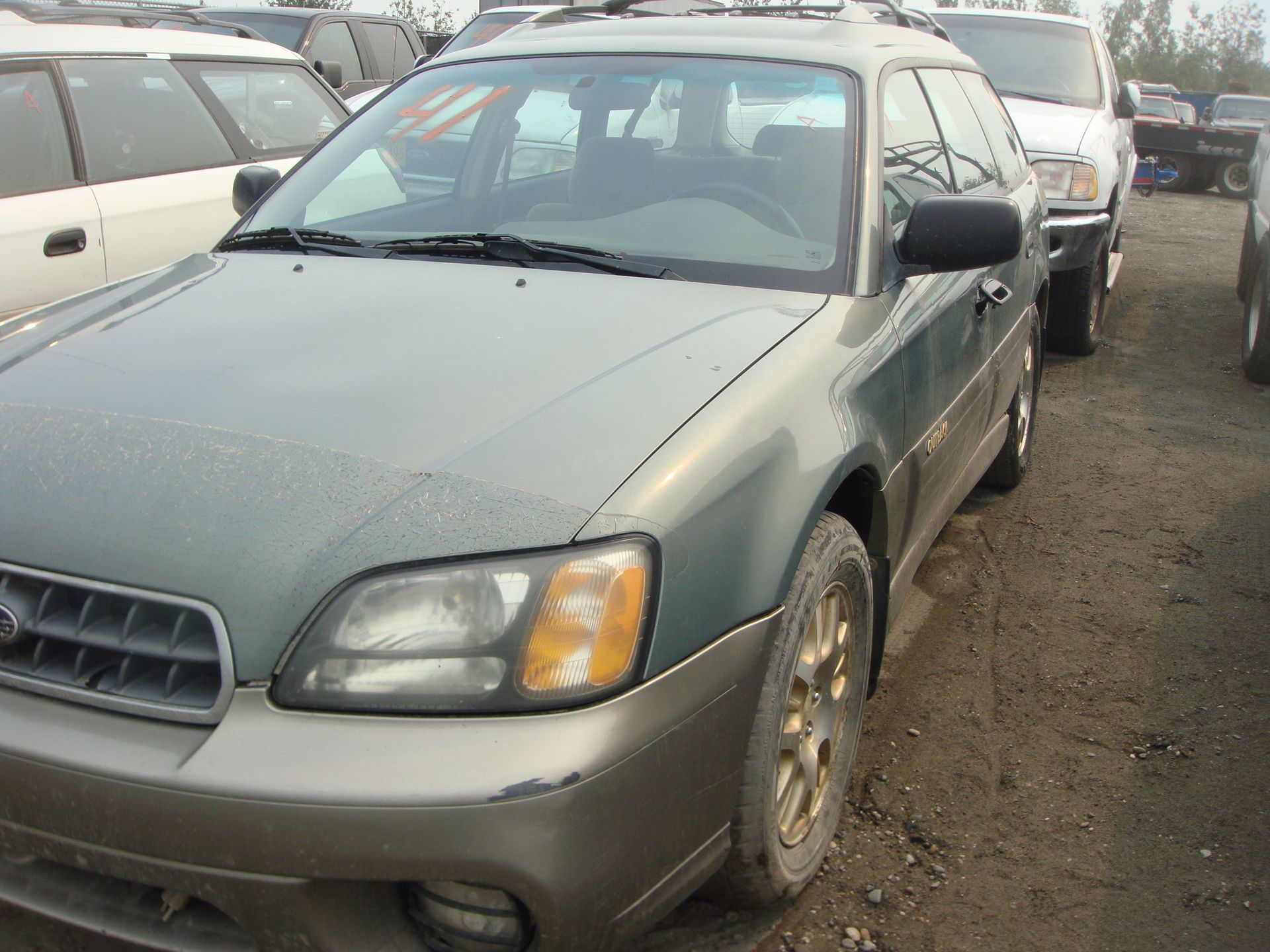 A green car is parked in a lot with other cars