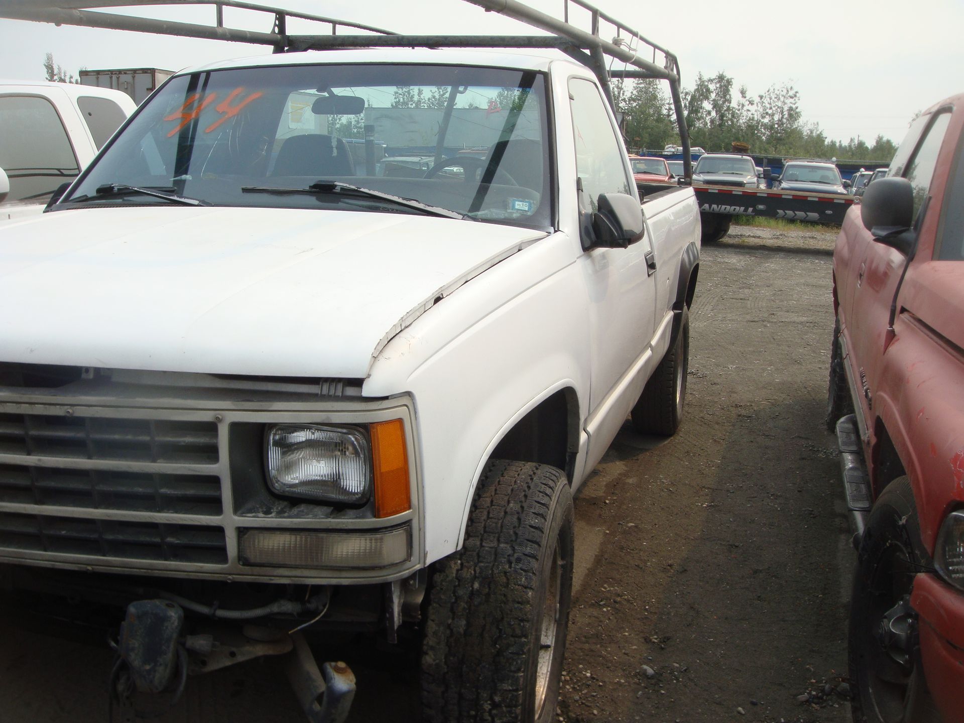 A white truck is parked next to a red truck