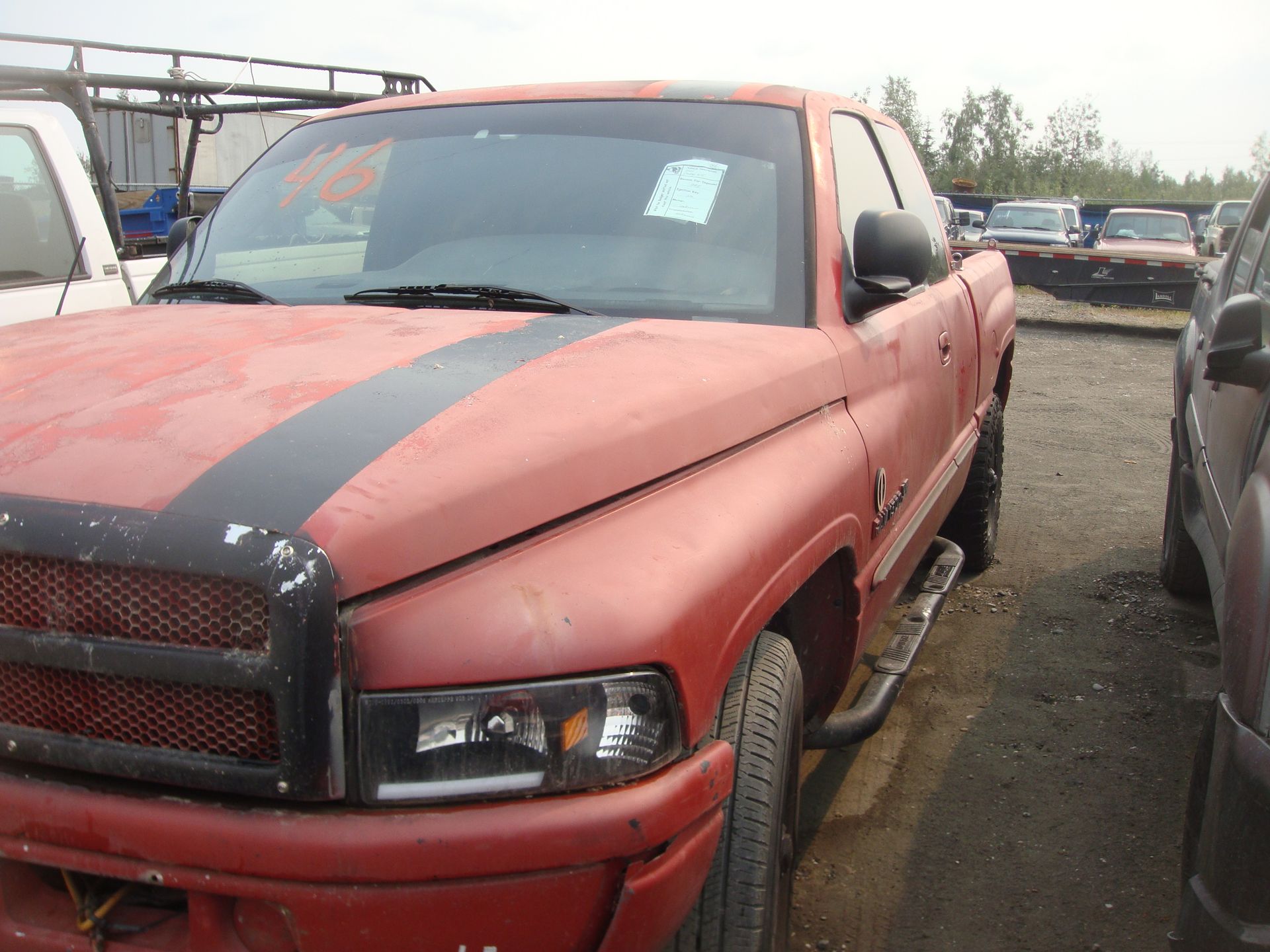 A red truck with a black stripe on the hood is parked in a lot