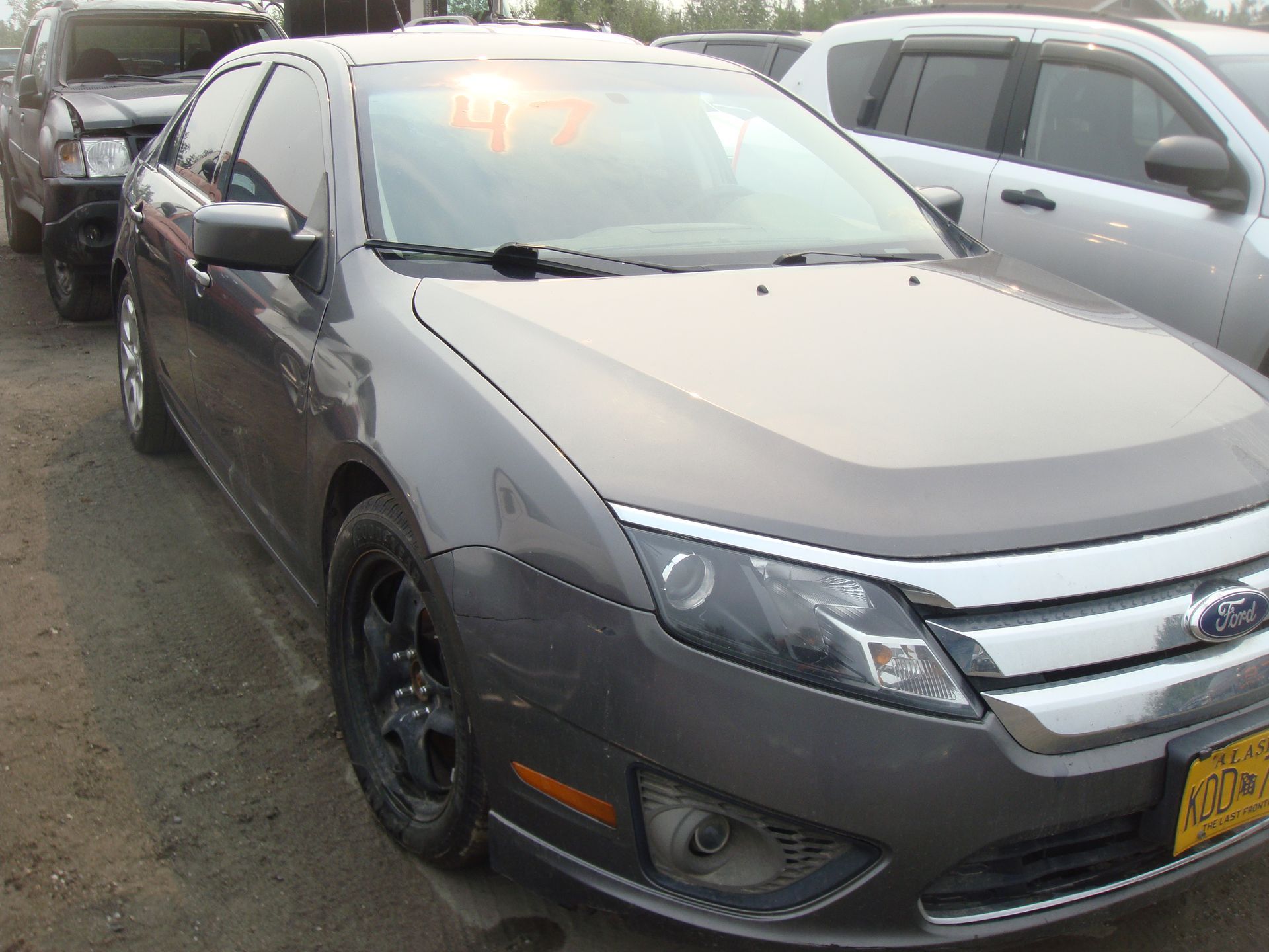 A gray ford fusion is parked in a lot with other cars.