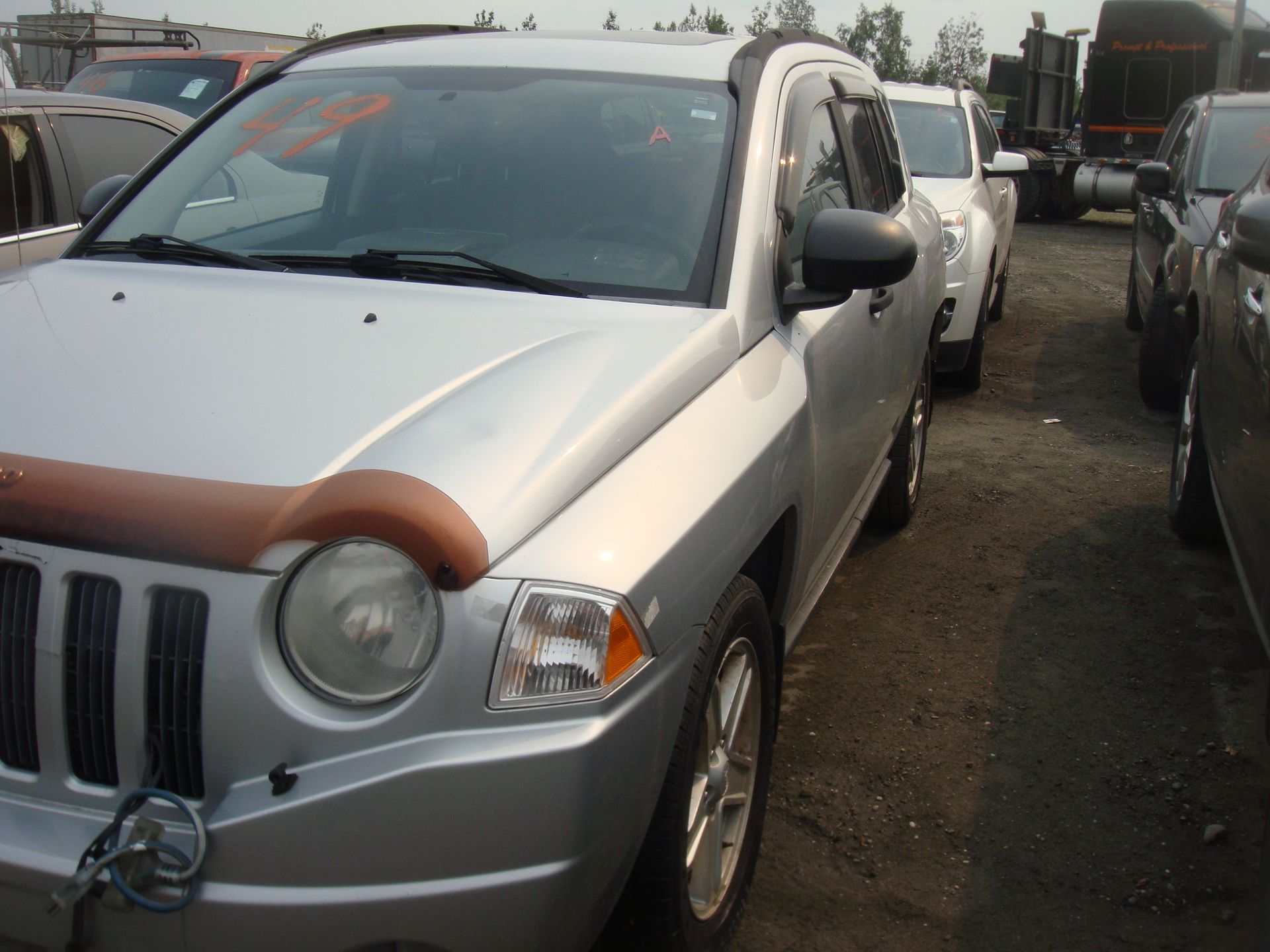 A silver jeep is parked in a lot with other cars