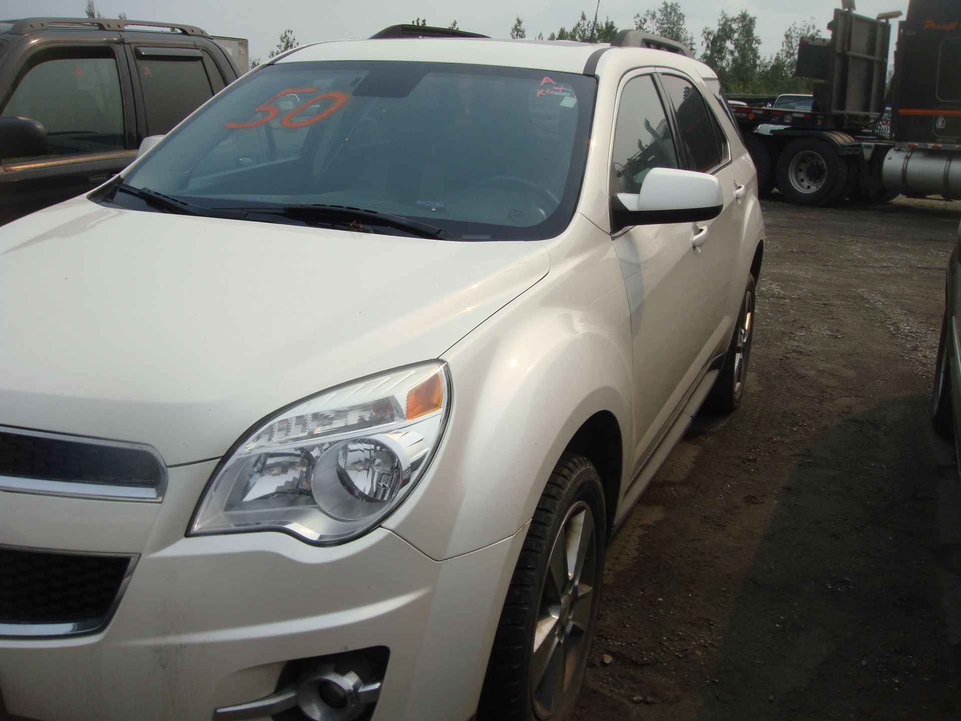 A white chevrolet equinox is parked in a gravel lot