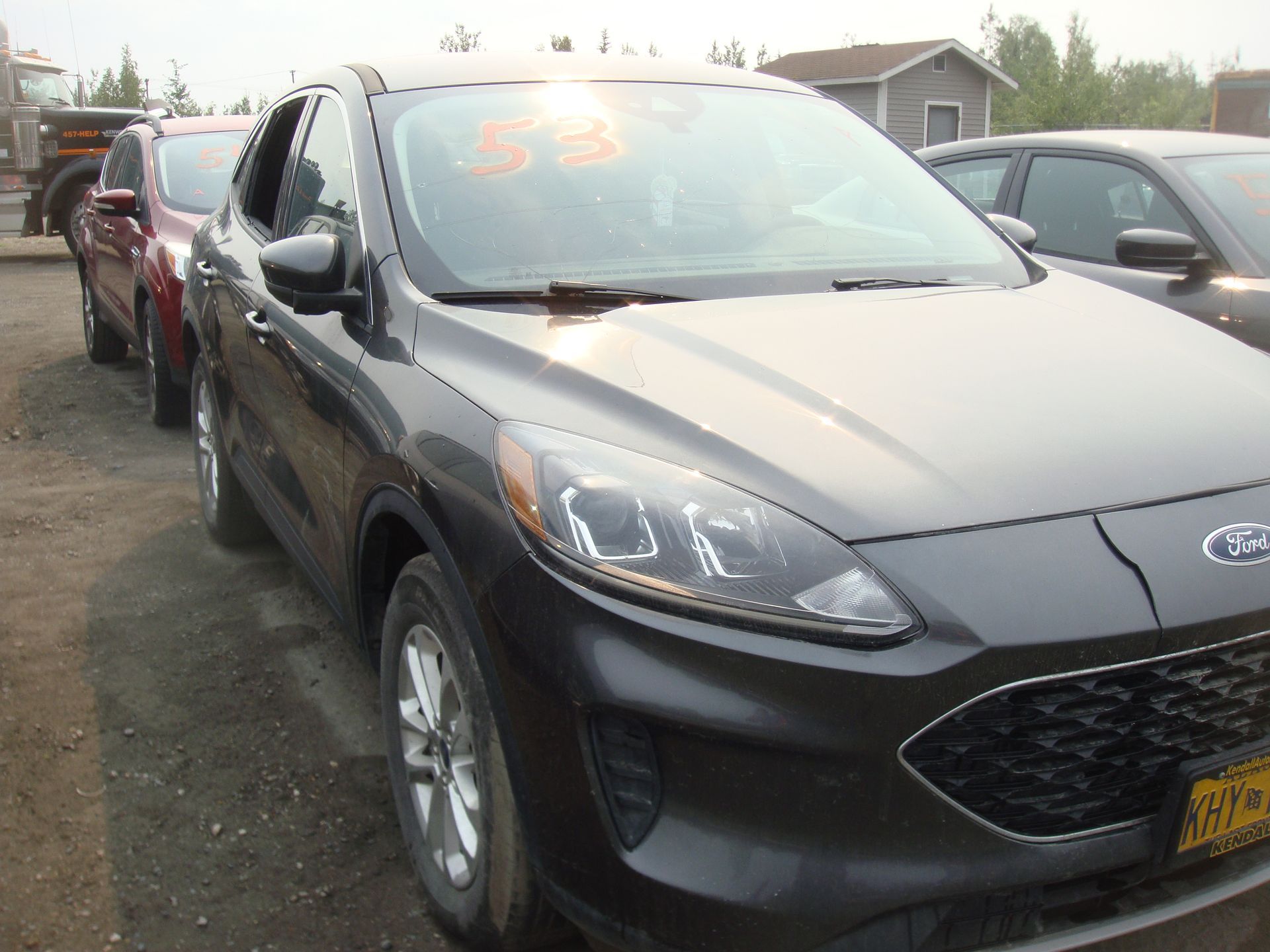 A black ford escape is parked in a lot with other cars.