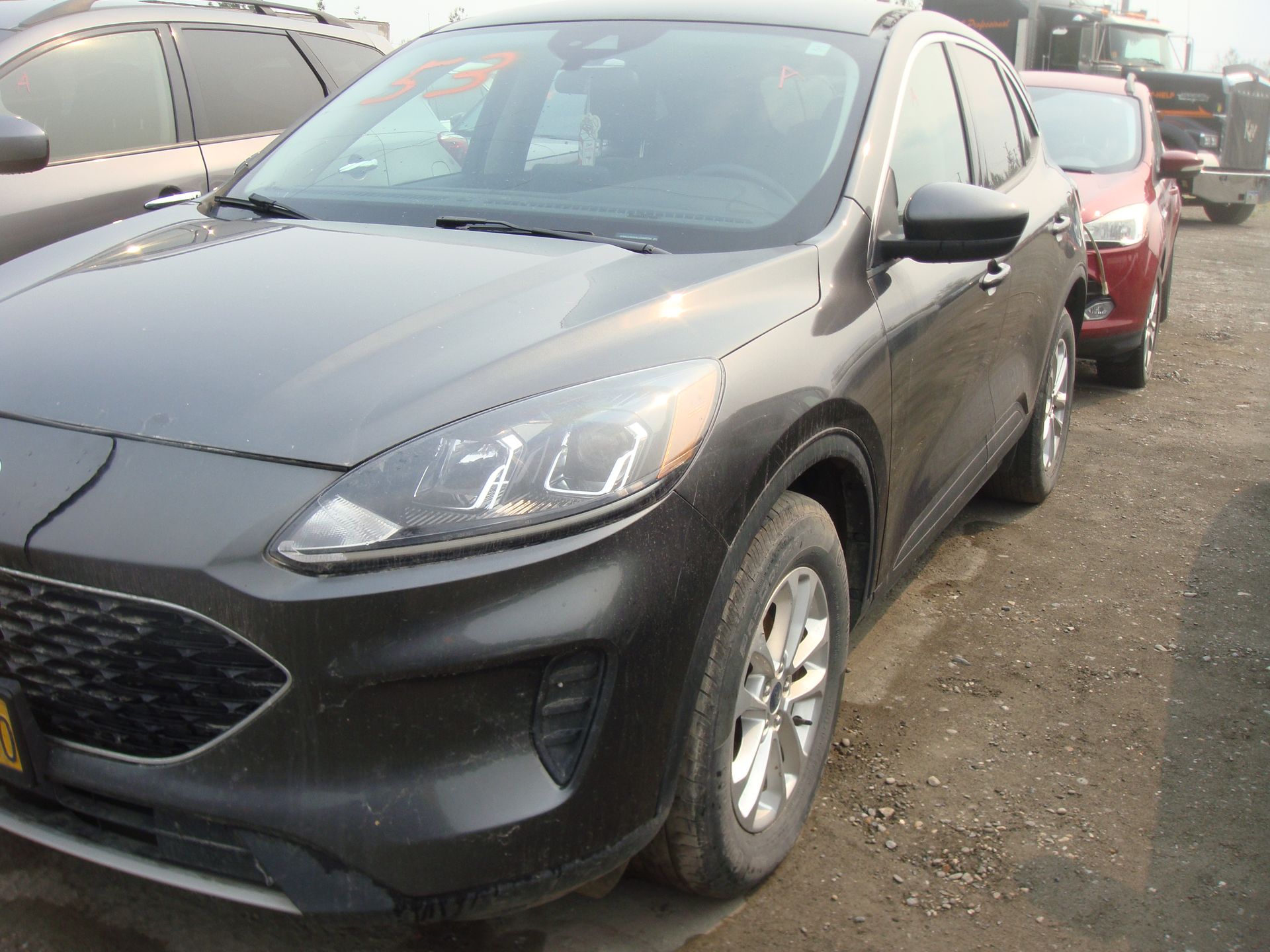 A black ford escape is parked in a lot with other cars.
