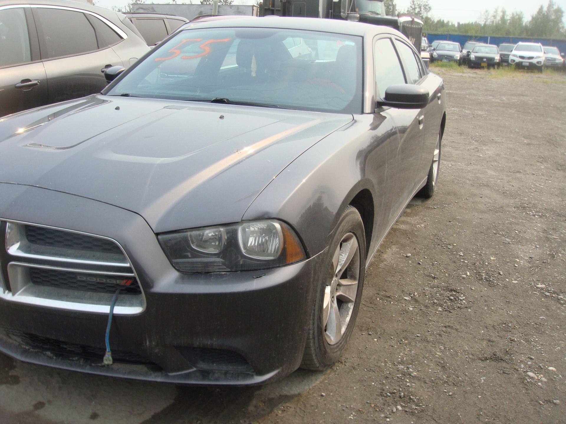 A gray dodge charger is parked in a gravel lot
