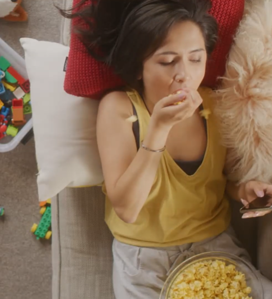 A woman is laying on a couch eating popcorn