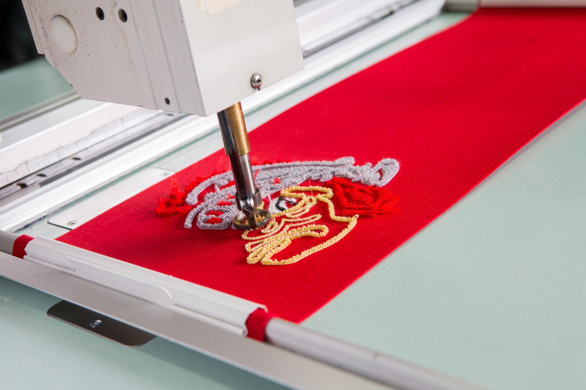 A custom Chenille patch beginning to be sewed into red fabric.