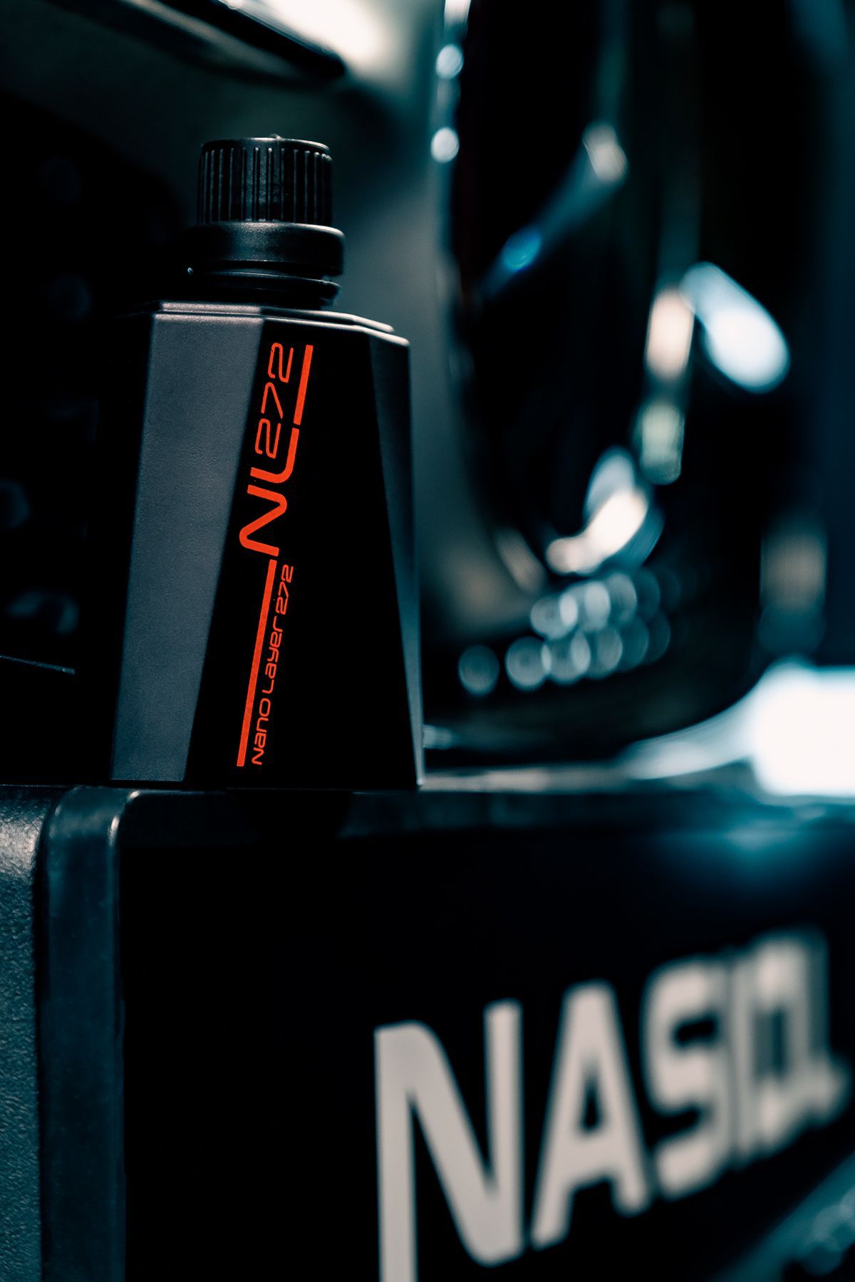 Black bottle of NUZU car care product on a NASIOL surface. Neon orange text.