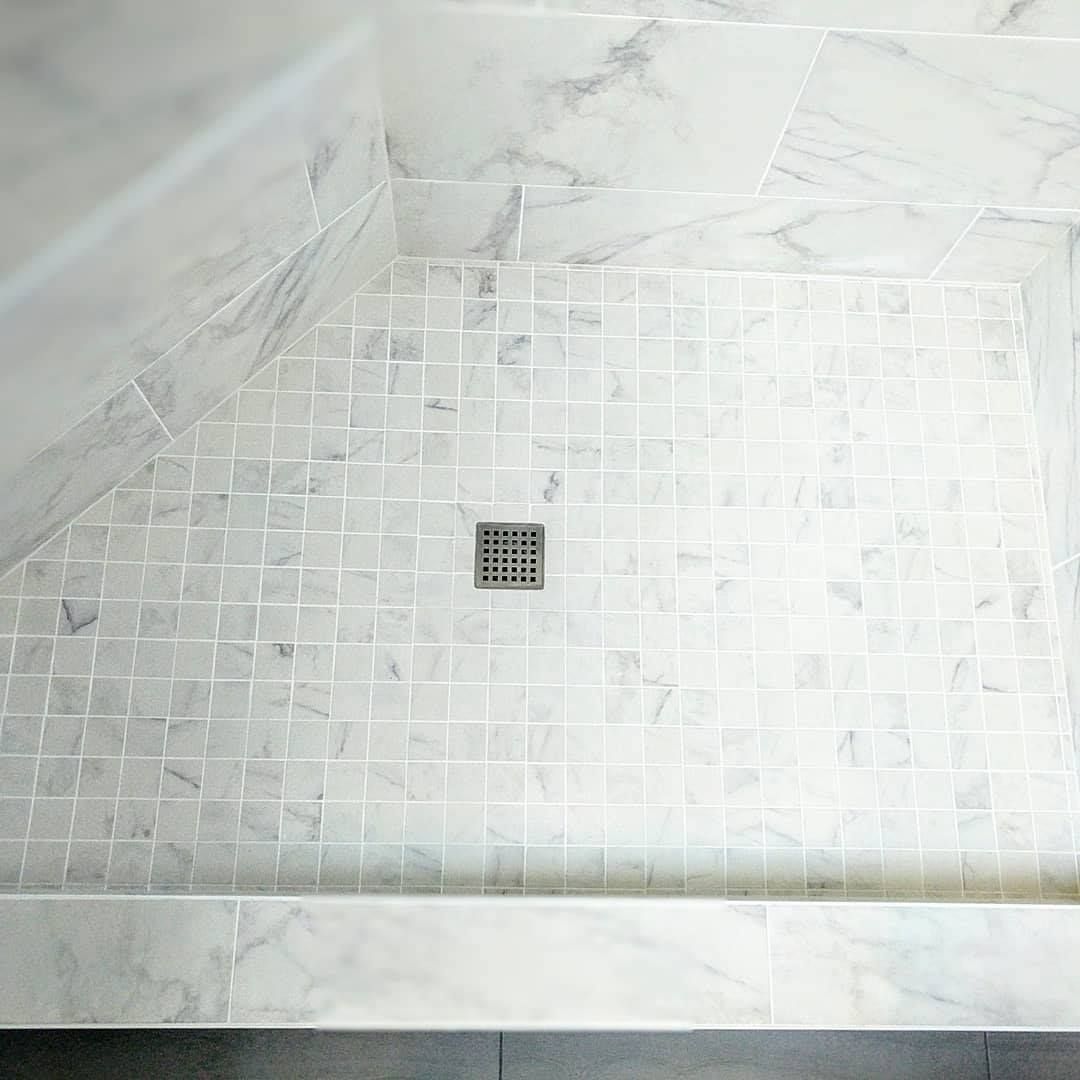 A shower stall with white tiles and a drain in a bathroom.