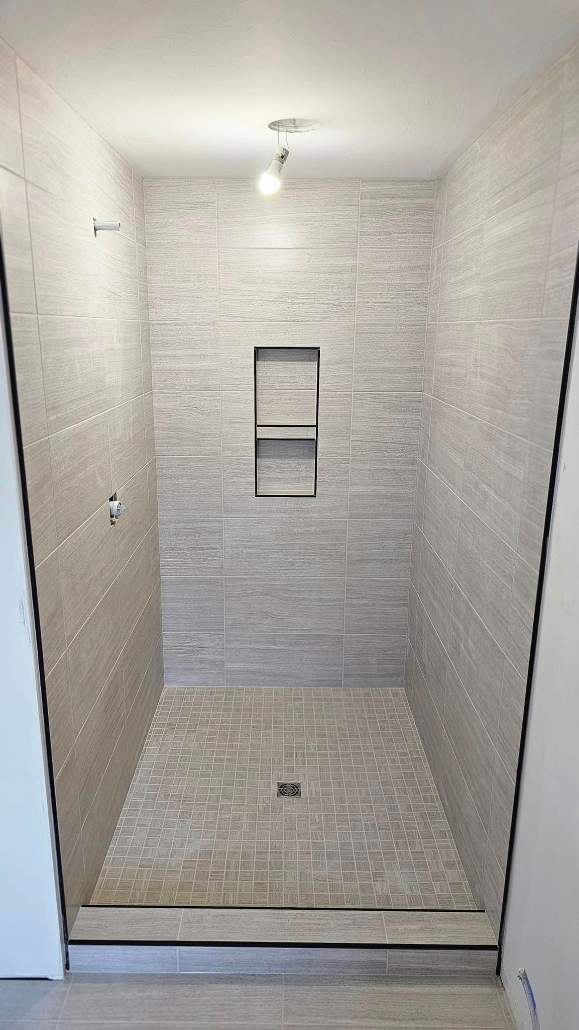 A walk in shower with a glass door and a shelf in the wall.