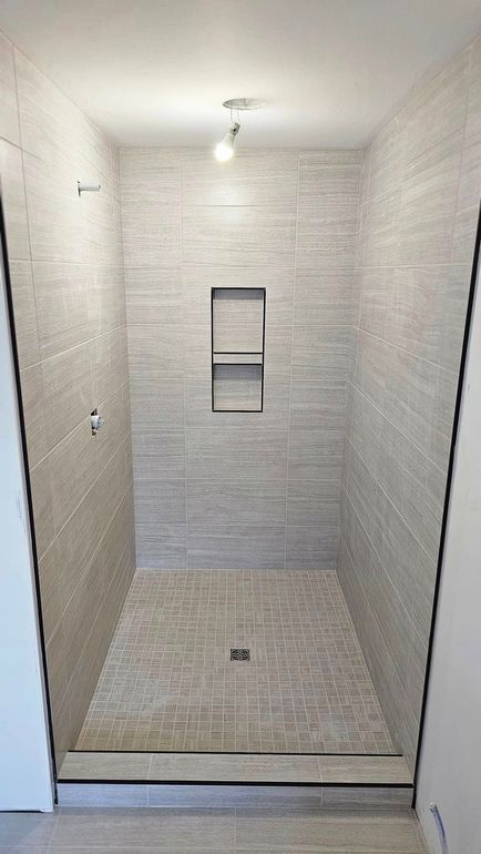 A walk in shower with a glass door and a shelf in the wall.