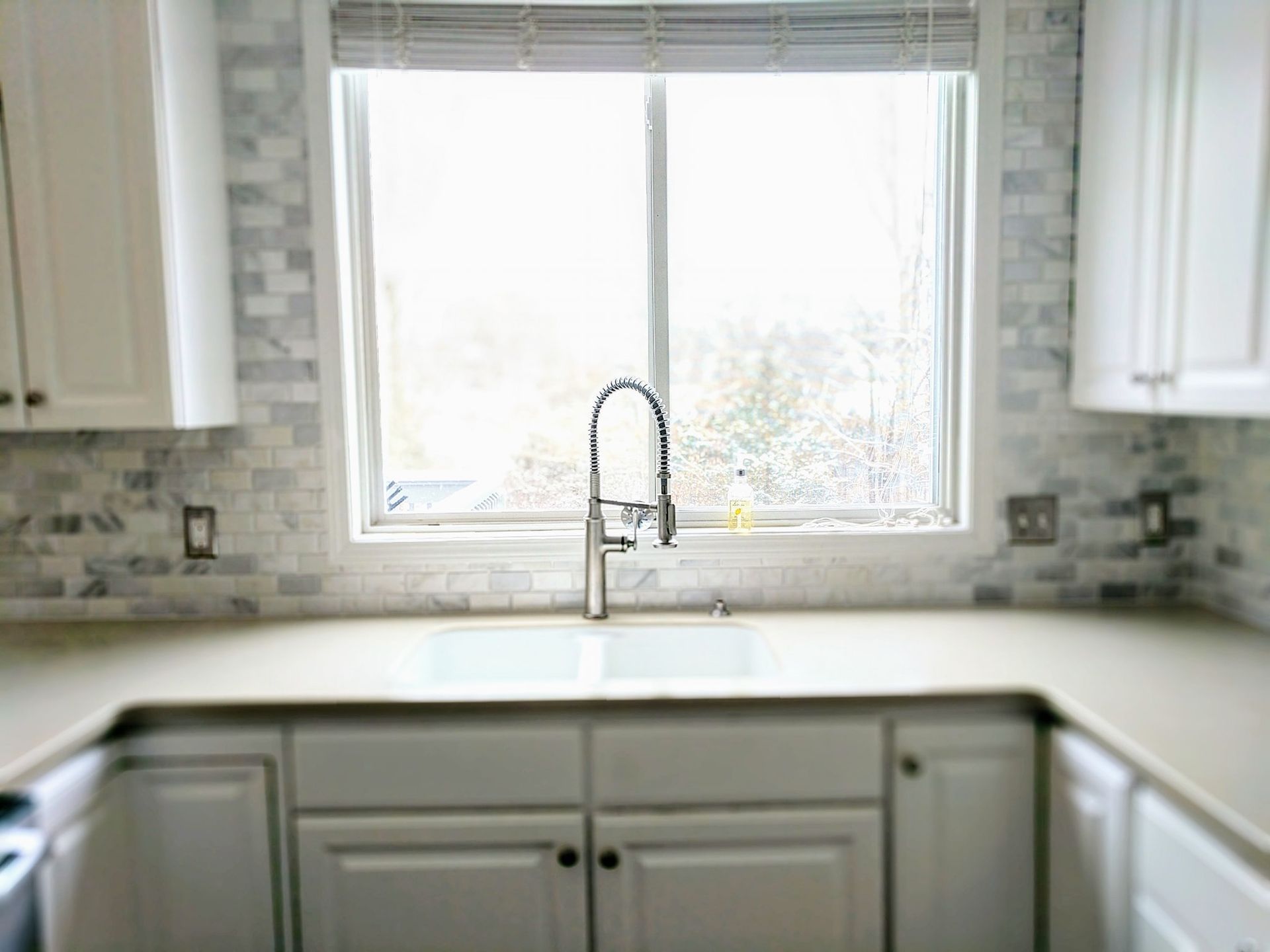 A kitchen with white cabinets , a sink , and a window.