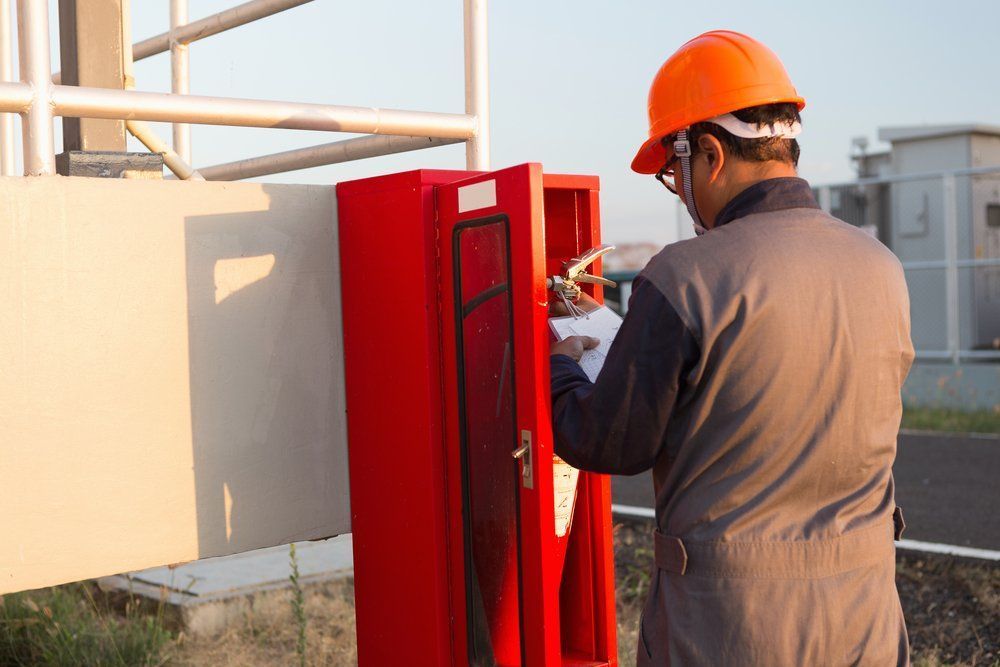 Worker In Orange Hard Hat Checking A Red Fire Extinguisher Box Outdoors — Wendy's Safety Services in Moulden, NT