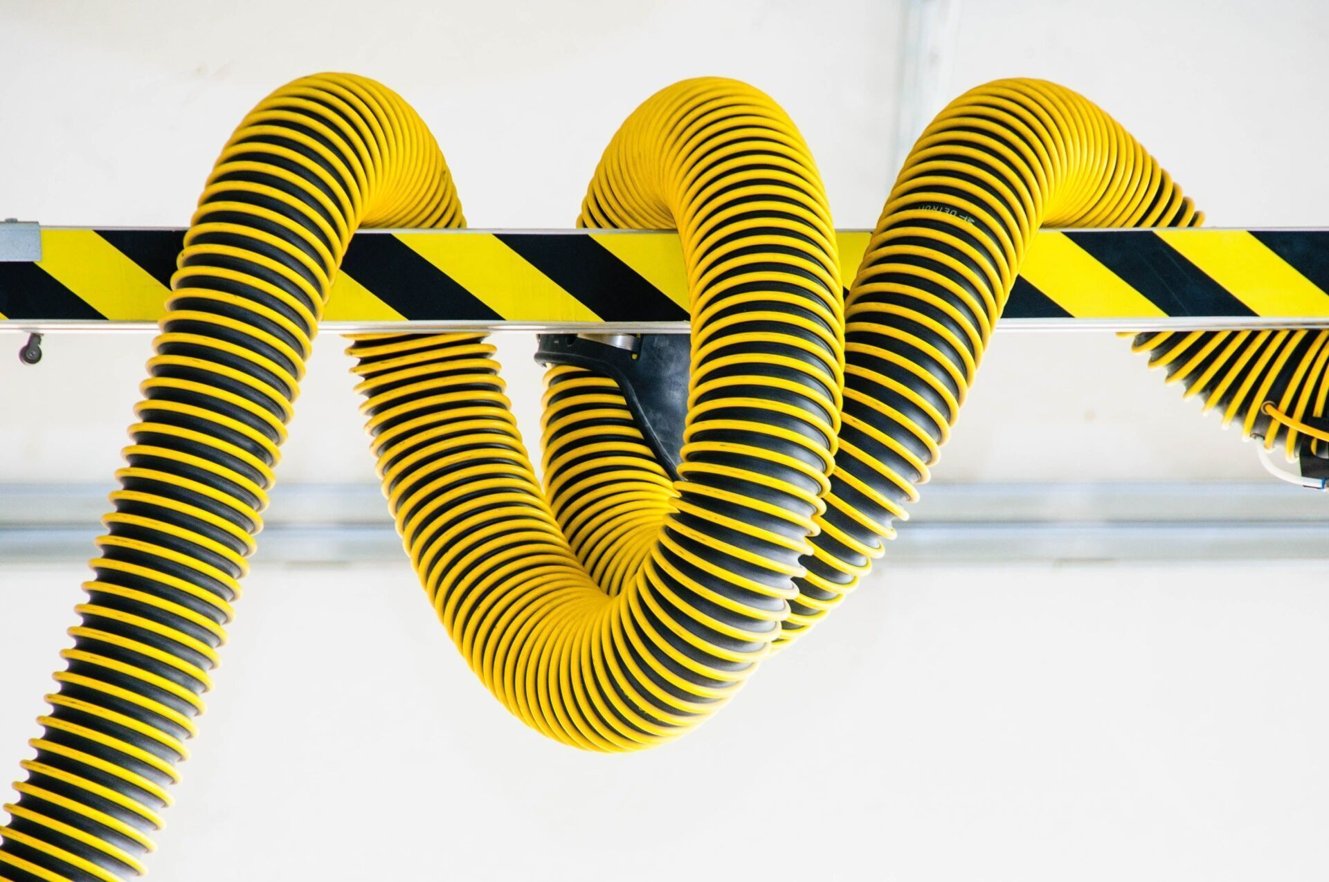 Yellow And Black Corrugated Hose Suspended From A Ceiling Beam — Wendy's Safety Services in Nhulunbuy, NT