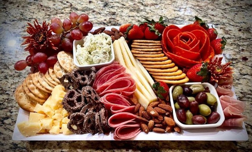 A white plate topped with meat , cheese , crackers , nuts , grapes and strawberries.