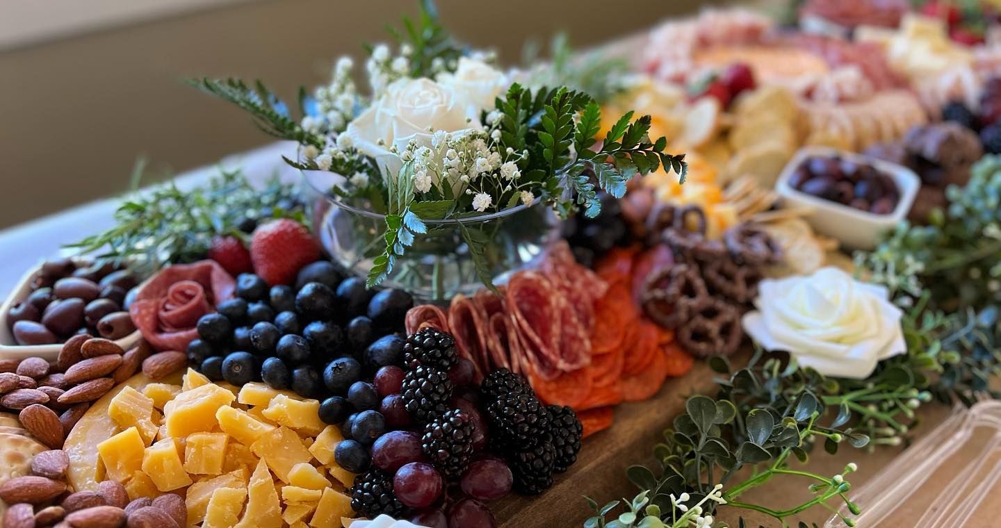 A wooden cutting board filled with lots of different types of food and flowers.