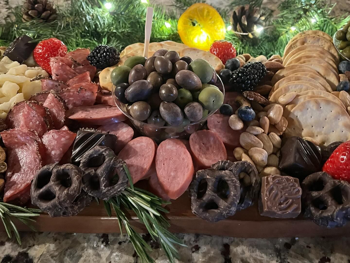 A wooden cutting board filled with meats , nuts , pretzels , berries and crackers.